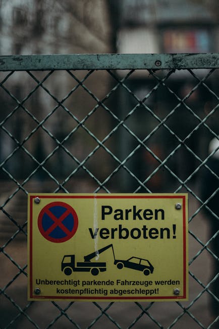 A black-and-white photograph showing a large rectangular 'Road Closed' sign positioned on a muddy ground in front of a construction site or roadworks area. Behind the sign, there is a metal fence with